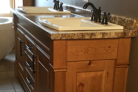 Custom knotty pine base cabinet and matching mirror frames. Square posts with false doors and laminated countertop with drop-in sinks. Furniture-style design.